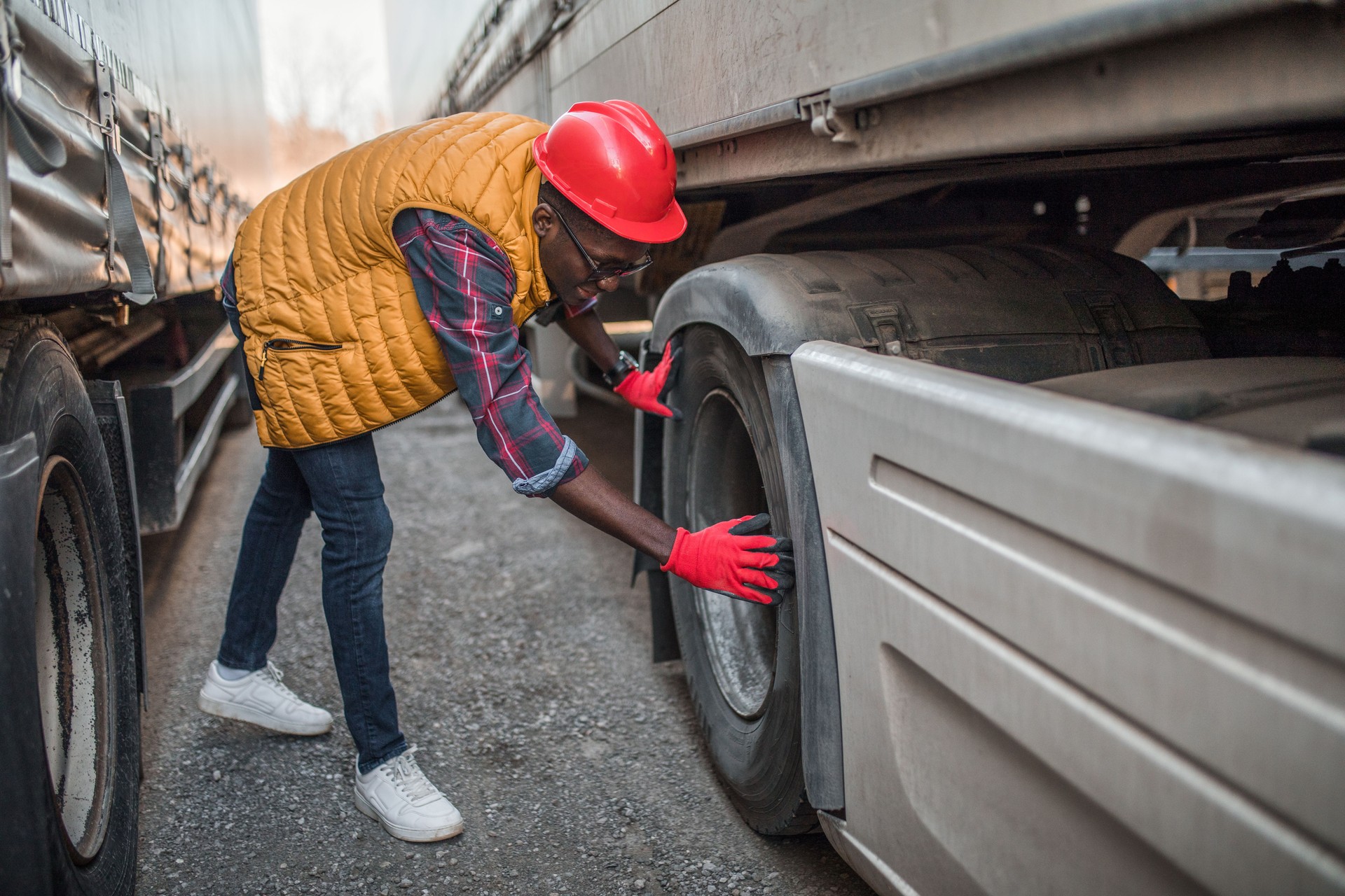 Black male truck driver with protective headwear inspecting tires